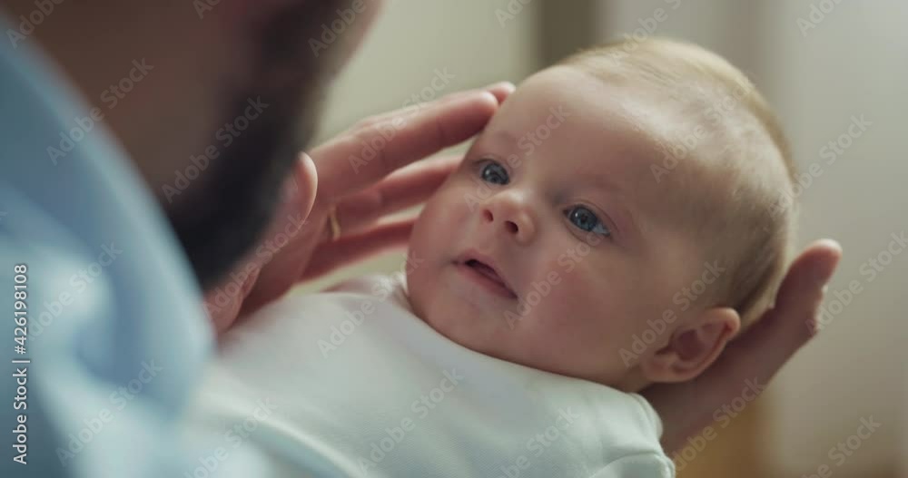 Cinematic close up shot of young neo father is playing with his newborn baby in a nursery in a morning. Concept of children, baby, parenthood, childhood, life, love, fatherhood, family.
