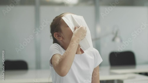 A pretty little girl child picks up a white napkin from the table and blows her nose into it