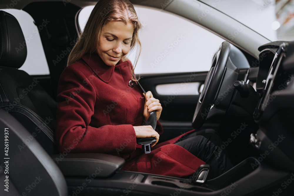 Smiling woman fasten seat belt before driving.