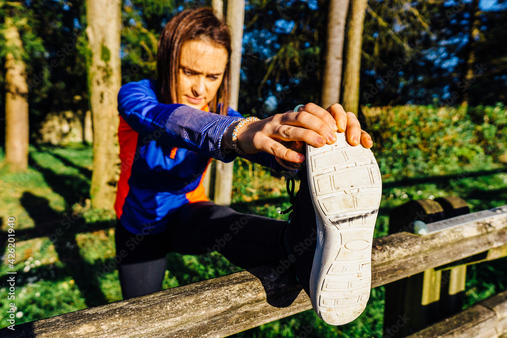 Obraz premium Young woman beautiful adult stretching her hamstrings touching her toes in a wooded park at sunset point concept sport weekend afterwork