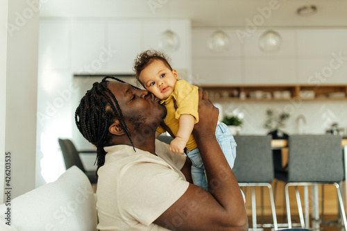 Portrait of an african american dad holding and kissing his daughter.