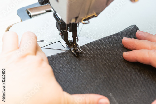 A woman seamstress sews a black cloth on an industrial sewing machine