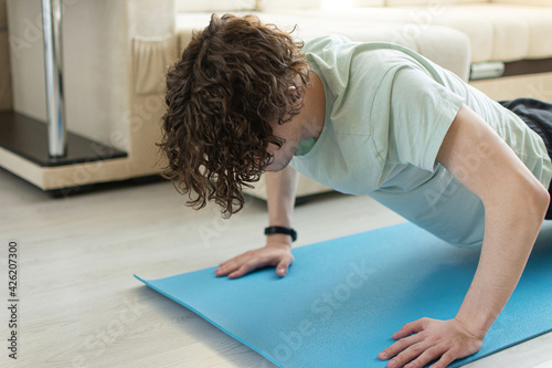 The concept of a cheerful and healthy start the day before working remotely.An adult Caucasian curly-haired man doing push-ups from a floor while on a yoga mat with a heart rate monitor on his arm.