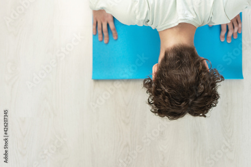 The concept of a healthy body in a home environment. An adult Caucasian curly-haired, long-haired man stands upright on a Yoga mat that lies on a wooden floor. View from above. copy space. close-up