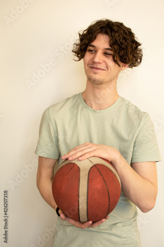 The concept of posing a model on the territory of her own apartment. A Caucasian, curly-haired, stubble adult man poses with a rubber basketball with one hand on the ball. Looking out of the camera.