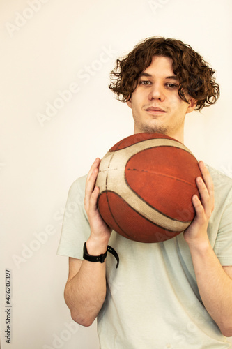 The concept of sports, healthy behavior inside. An adult curly-haired Caucasian man stands with a basketball in his hands, a gadget for measuring heart rate on his arm, arms bent at the elbows.