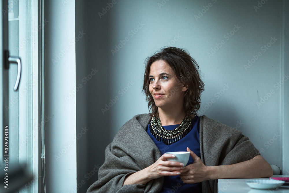 A woman sitting near the window of her house. A woman sitting near the window of her house.