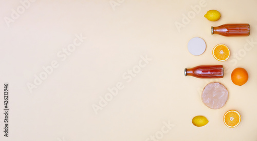 Horizontal banner with two bottles of kombucha tea, scoby and fruits for additional flavors on yellow pastel background. Orange, lemon, apple. Healthy fermented drink. Flatlay mockup, copy space