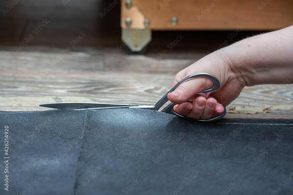 Woman's hand cuts black covering material on the floor with scissors Woman's hand cuts black covering material on the floor with scissors