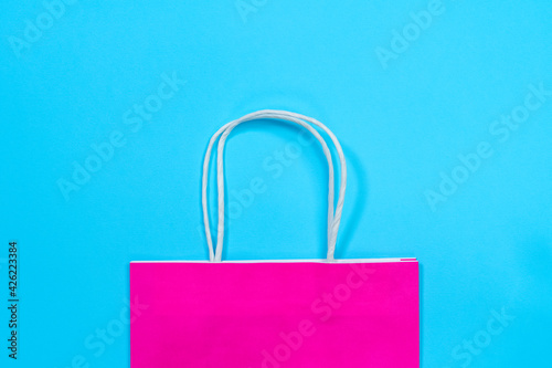 Half of acid pink eco-friendly shopping paper bag with handles made of recyclable material for packaging and carrying goods, blue background, top view, copy space.