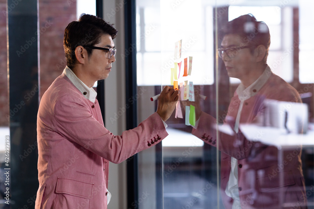 Stylish asian businessman writing notes on glass wall Stylish asian businessman writing notes on glass wall