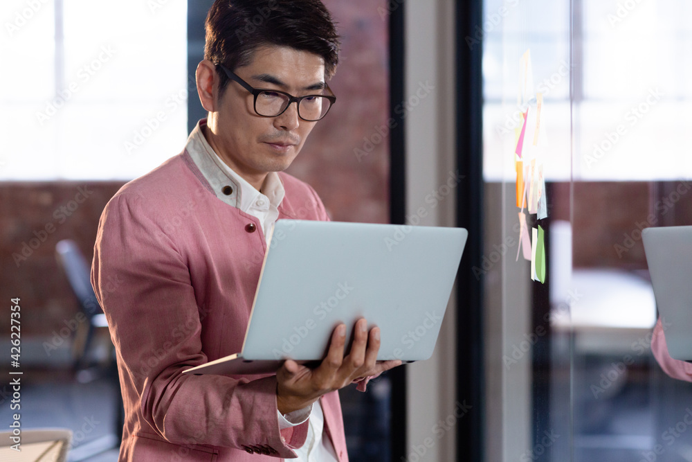Stylish asian businessman standing and using laptop computer Stylish asian businessman standing and using laptop computer