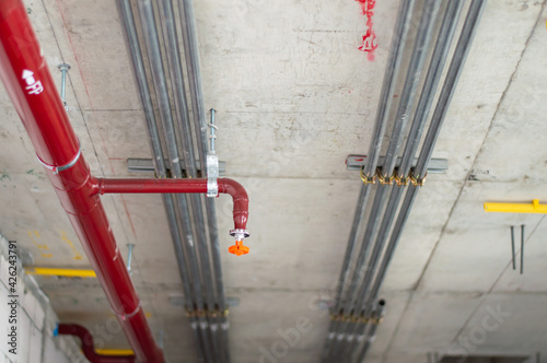 Fire sprinkler system with red pipes is placed to hanging from the ceiling inside of an unfinished new building.Installation of conduits in buildings.Conduit system in building under construction.