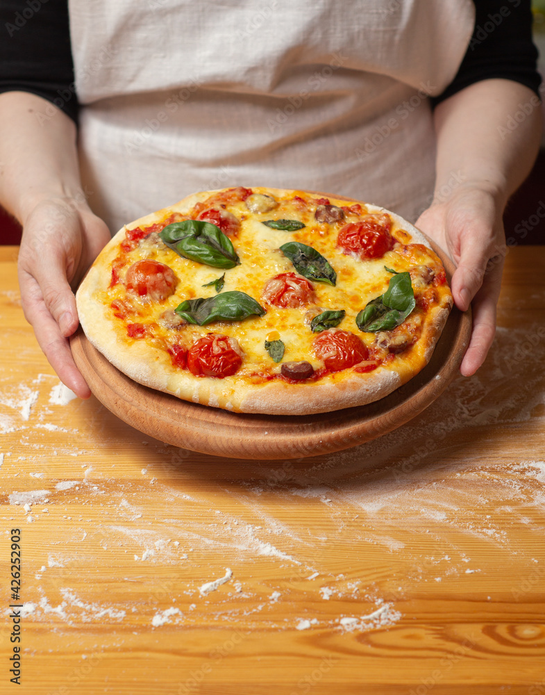 Chef holds wooden tray or board with homemade cheese pizza with tomato cherry, sauce, sausage and basil. Tasty dinner, close up view