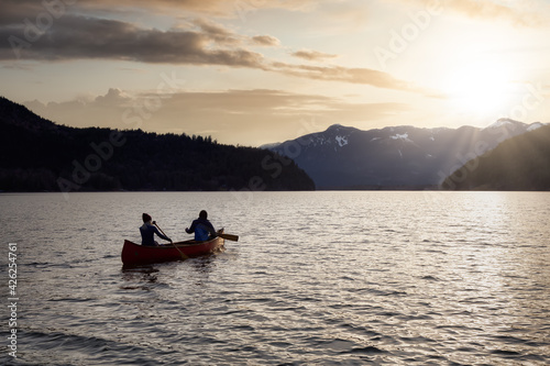 Couple friends canoeing on a wooden canoe during a colorful sunny sunset. Cloudy Sky Artistic Render. Taken in Harrison River, East of Vancouver, British Columbia, Canada.