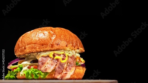 Craft burger is cooking on black background. Consist: sauce, lettuce, tomato, red onion, cucumber, cheese, bacon, air bun and breast of chicken. photo