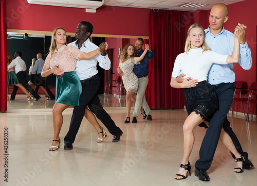 Positive adult couples dancing salsa dance together in modern studio