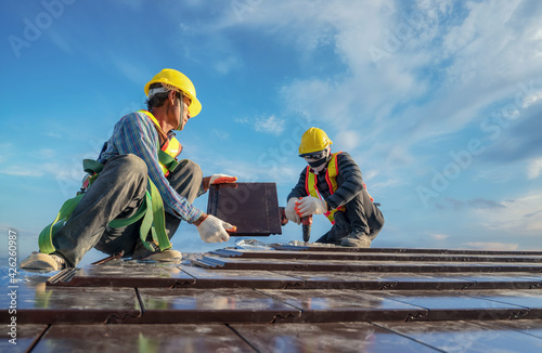 Foto Roofer installing ceramic roof tile on top roof by using air pneumatic nail gun