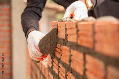 Close up hand of industrial bricklayer in glove installing bricks on construction site photo