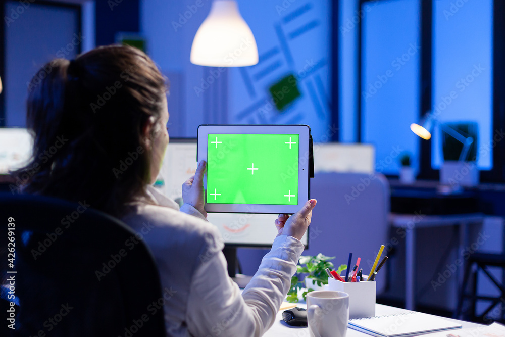 Manager woman holding tablet with green screen monitor during online web conference. Entrepreneur looking at desktop monitor display with green mockup, chroma key sitting at desk in business office Manager woman holding tablet with green screen monitor during online web conference. Entrepreneur looking at desktop monitor display with green mockup, chroma key sitting at desk in business office