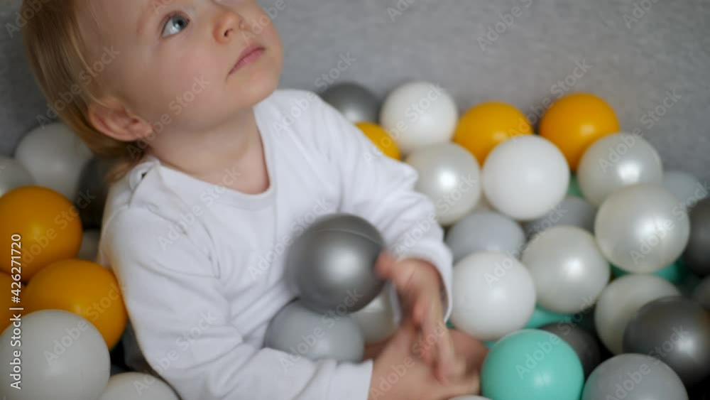 girl in a white bodysuit plays with colorful plastic balls in dry pool girl in a white bodysuit plays with colorful plastic balls in dry pool