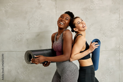 Young cheerful athletic women holding Yoga mats and laughing against the wall. photo