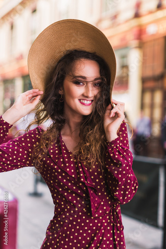 Portrait of a stylish woman in a hat and polka dot dress. Beauty. Polka dot dress. Burgundy in polka dots. Background of vintage shops.