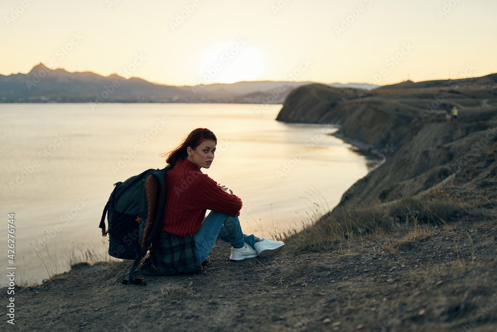 a traveler with a backpack looks at the sunset at the sea in the mountains