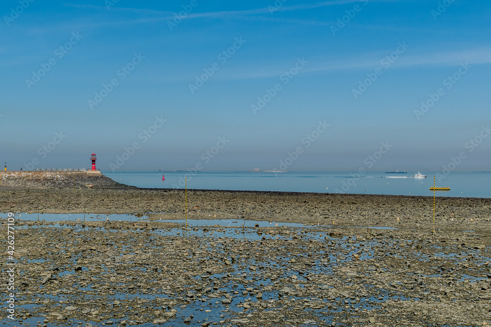 Rocky beach at low tide with red lighthouse at end of concrete pier.