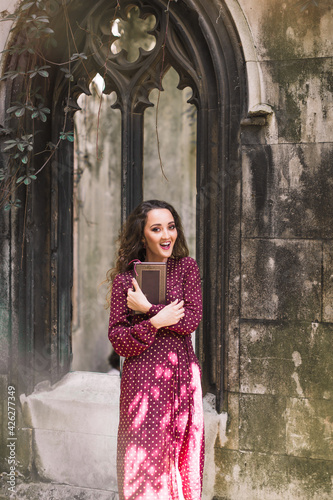 Stylish woman in a polka dot dress. Holds a book. Beauty. Polka dot dress. Burgundy in polka dots. Background architecture. Gothic architectures.