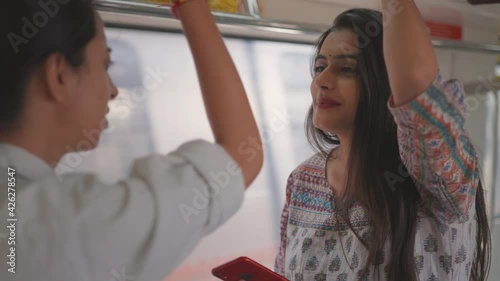 front view close shot of a happy and beautiful young Indian woman in traditional dress commuter standing and having a conversation with a fellow passenger in a  moving metro train