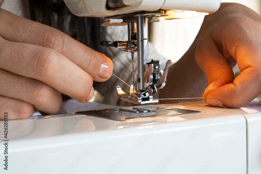 young woman putting thread on needle of sewing machine