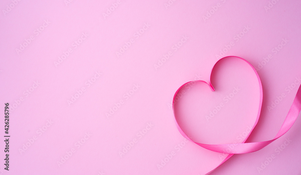 Pink ribbon folded in the shape of a heart on a pink background. Love and valentine's day concept