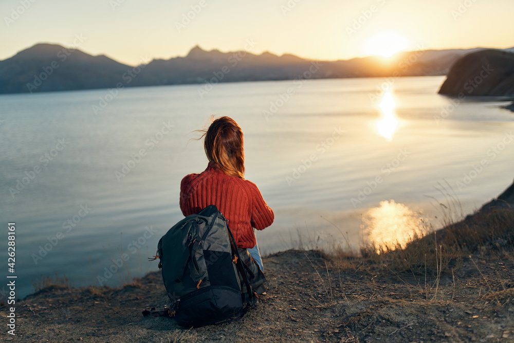 a traveler in a sweater Sits on the seashore and watches the sunset