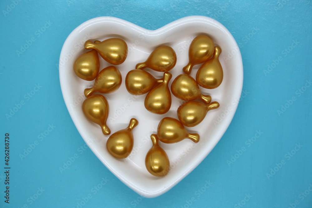 Capsule gold oil for face in the white plate in the shape of a heart.