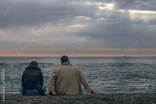 young couple sitting on the beach on the background of the sea back view © Mikhail