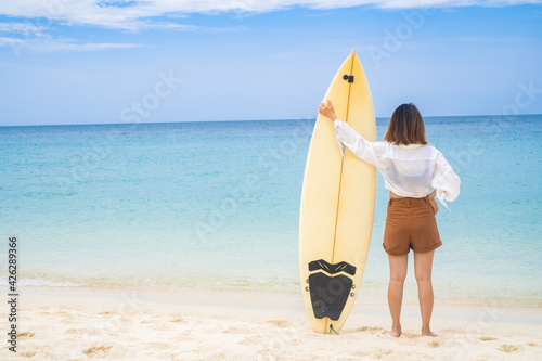 Photography Woman holding surfboard and standing in front of the beach