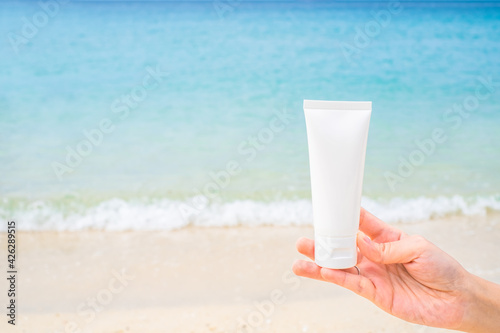 Female hand holding empty cosmetic skin care cream or sun block with sea beach background travel vacation accessory 