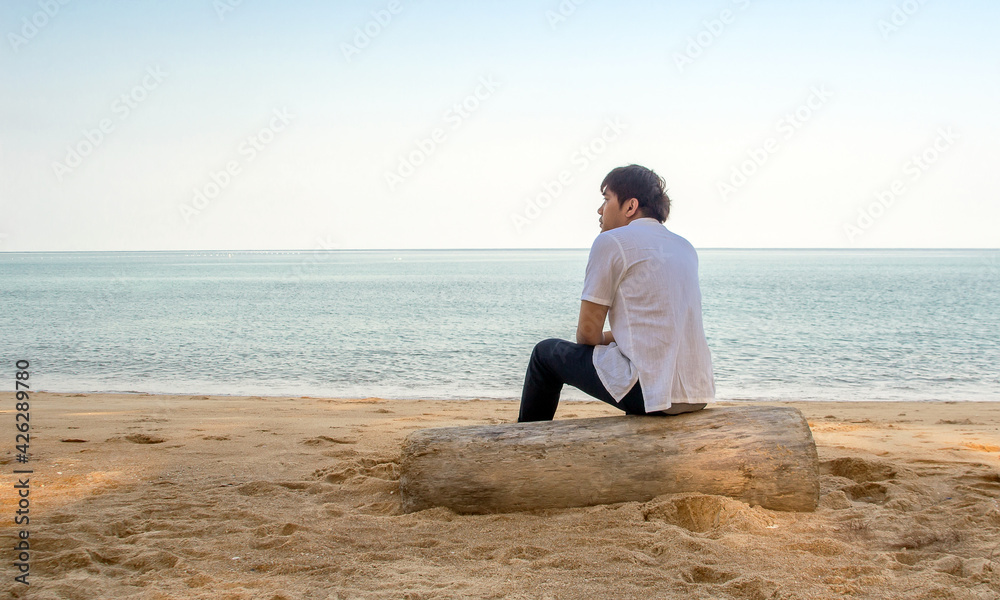 asian man sitting on wood log on the beach in holiday asian man sitting on wood log on the beach in holiday
