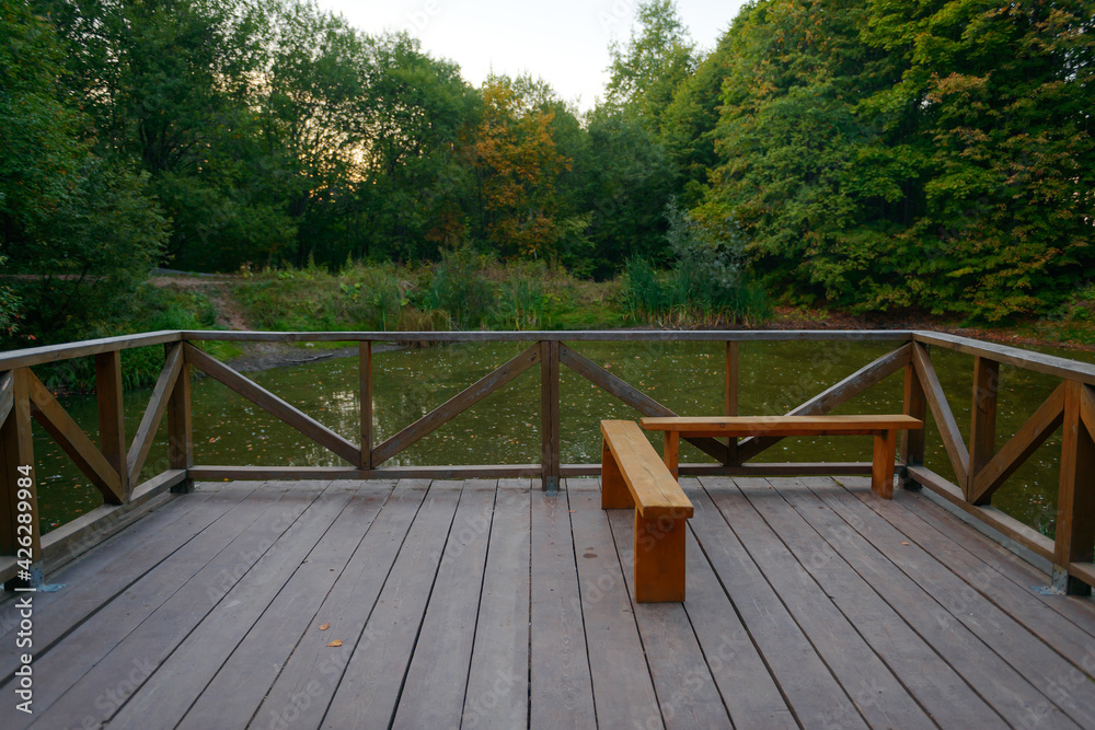 patio with a fence and a bench overlooking a small pond on a summer evening patio with a fence and a bench overlooking a small pond on a summer evening