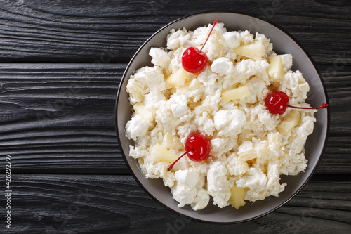 Foto Sweet salad of rice, marshmallows and pineapple dressed with whipped cream close-up in a plate on the table