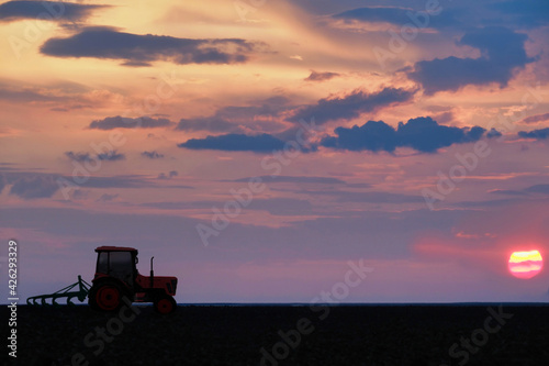 Colorful sunset landscape with tractor working on a field © emilio100
