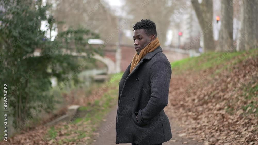 Serious black African man standing at park wearing winter clothing thinking about life Serious black African man standing at park wearing winter clothing thinking about life