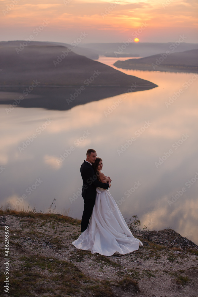 The groom sensual hugging bride in the mountains near the sea, amazing warm sunset The groom sensual hugging bride in the mountains near the sea, amazing warm sunset