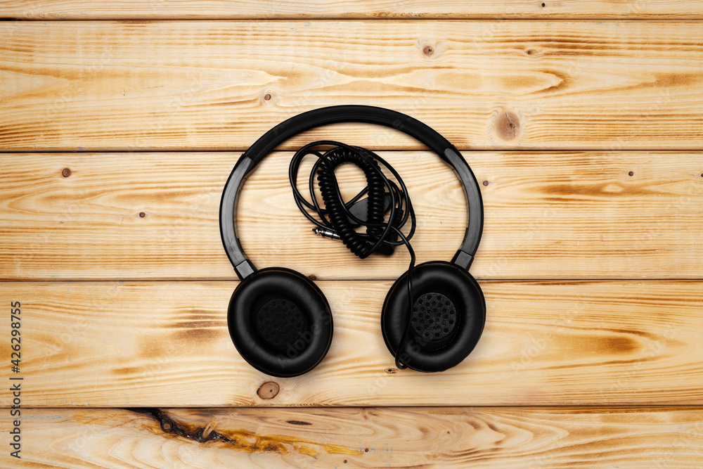 Black headphones with wire on wooden background Black headphones with wire on wooden background