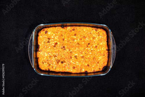 Cottage cheese casserole with raisins, carrots and dried apricots in a glass pan on a black tablecloth top view