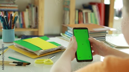  Phone with Green Screen and Chroma Key in the hands of a Primary school student.  Schoolboy Scroll Up Cellphone by Finger.  An elementary school student uses online videos to learn. 
