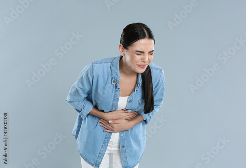 Woman suffering from stomach ache on grey background. Food poisoning photo