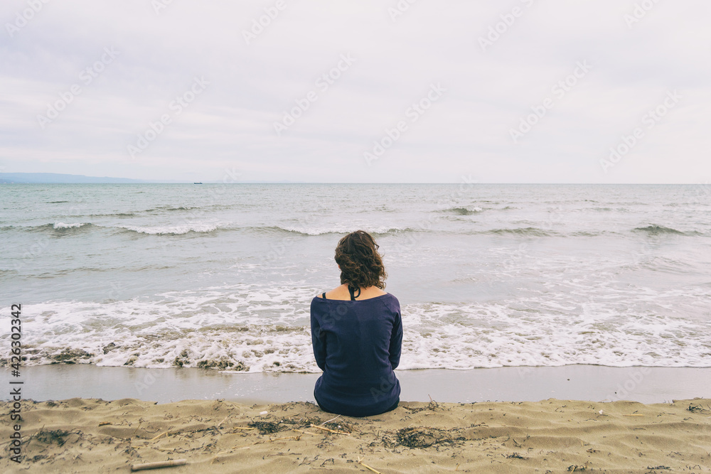 girl sitting on the sand on the shore of the beach looking at the horizon of the sea girl sitting on the sand on the shore of the beach looking at the horizon of the sea
