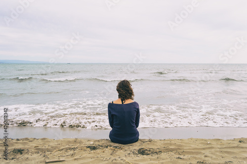 girl sitting on the sand on the shore of the beach looking at the horizon of the sea